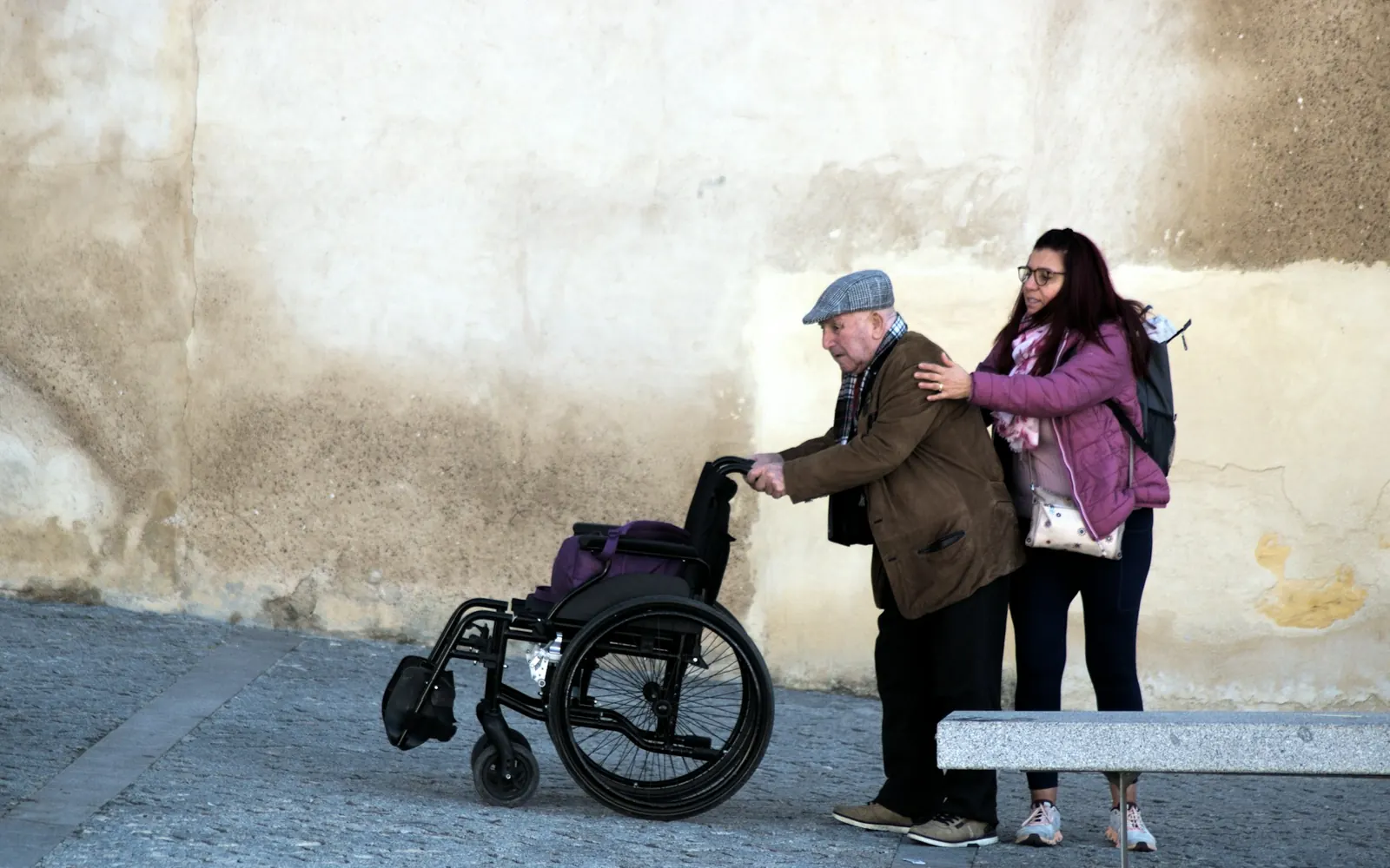 Jeune femme qui aide un homme âgé à marcher, un fauteuil roulant à côté d’eux