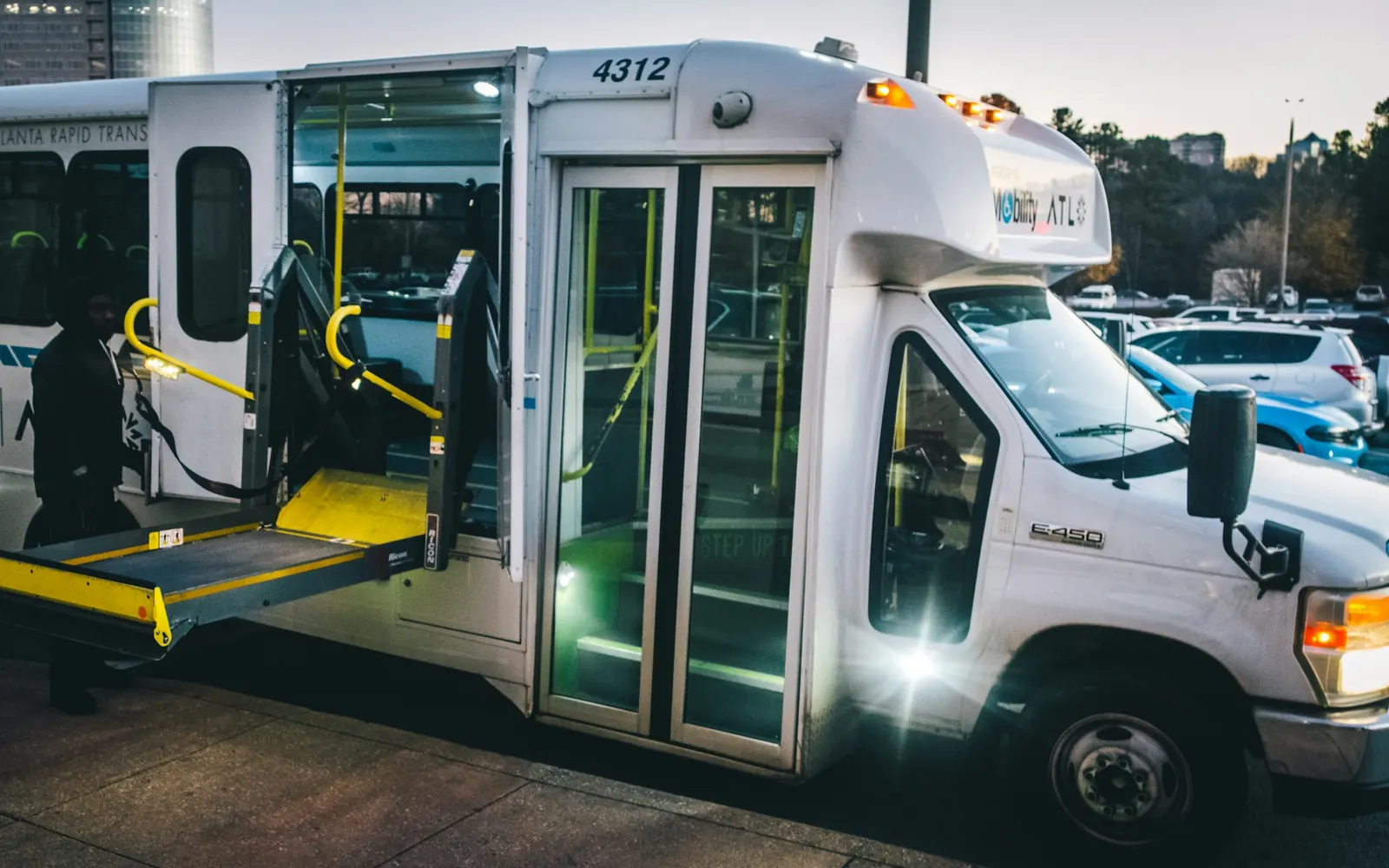 Minibus blanc de transport de personnes à mobilité réduite, portes arrière ouvertes et plateforme élévatrice dépliée, de nuit
