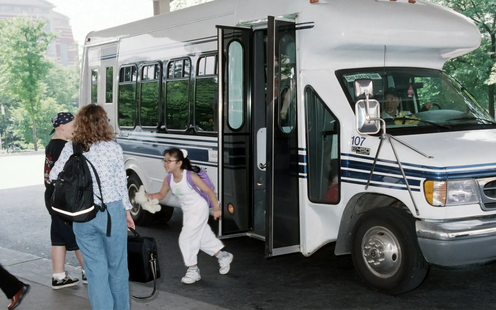 Minibus blanc avec plateforme élévatrice dépliée, passagers et accompagnants sur le trottoir avant un transport PMR