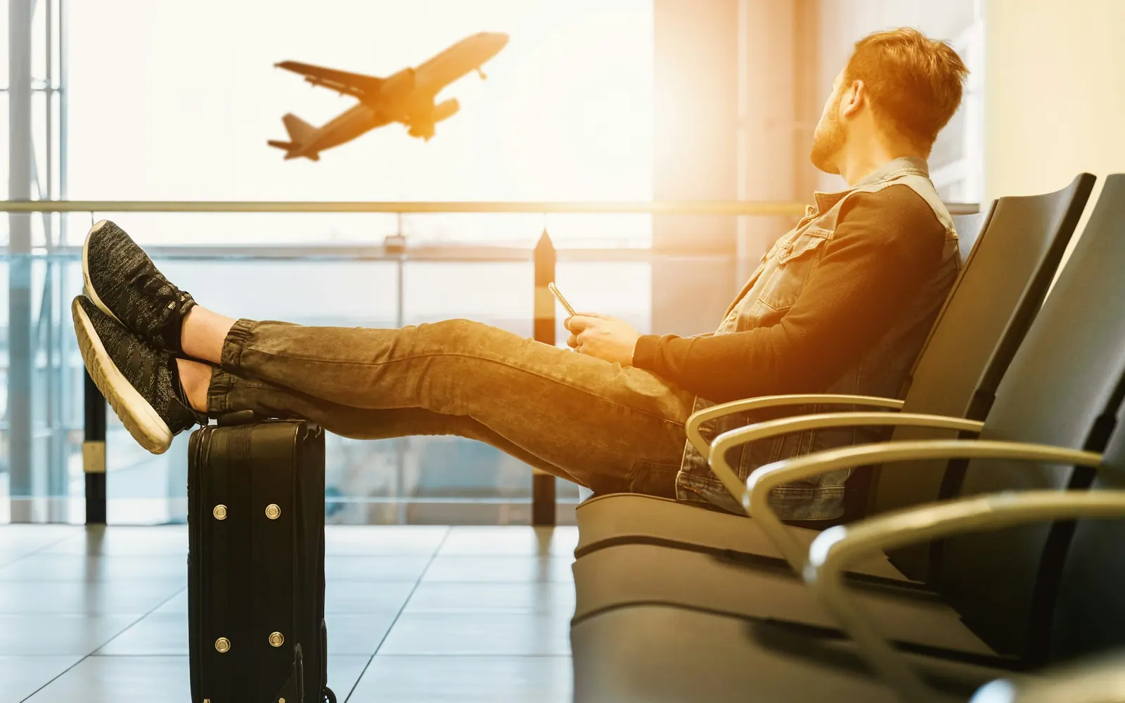 Voyageur qui attend dans un aéroport, avion au décollage derrière la vitre, avant une éventuelle absence passager